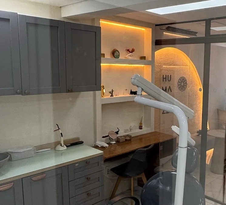Sala de atendimento com armários cinza, prateleiras iluminadas em âmbar, cadeira odontológica e parede curva com a marca Humanizze.
