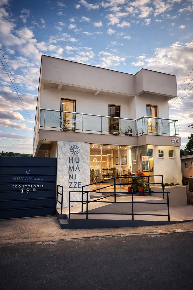 Fachada da Humanizze Odontologia ao entardecer: bloco de mármore com a palavra Humanizze, portão azul-escuro e vitrine iluminada.